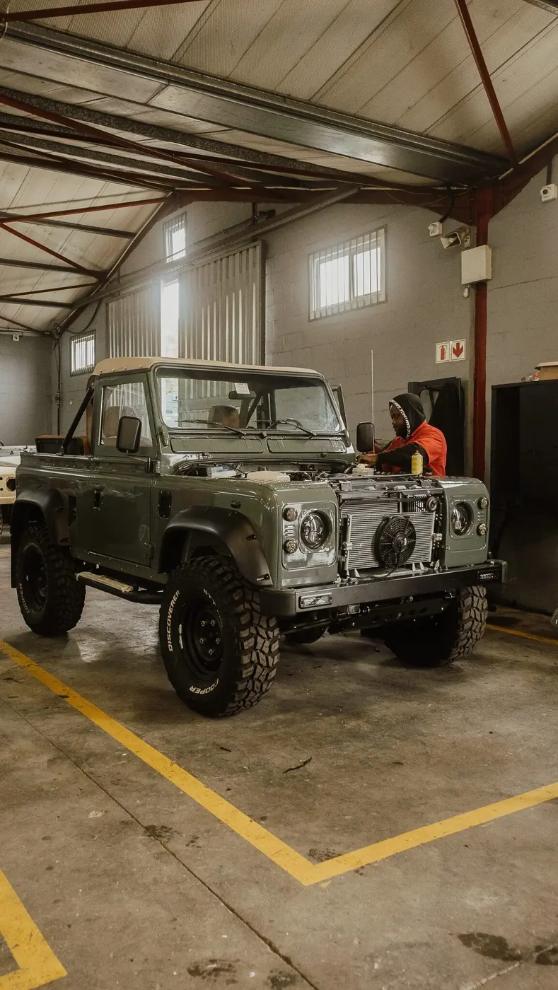 Green Land Rover Defender mid-build in the workshop, front panel off, with a technician at work