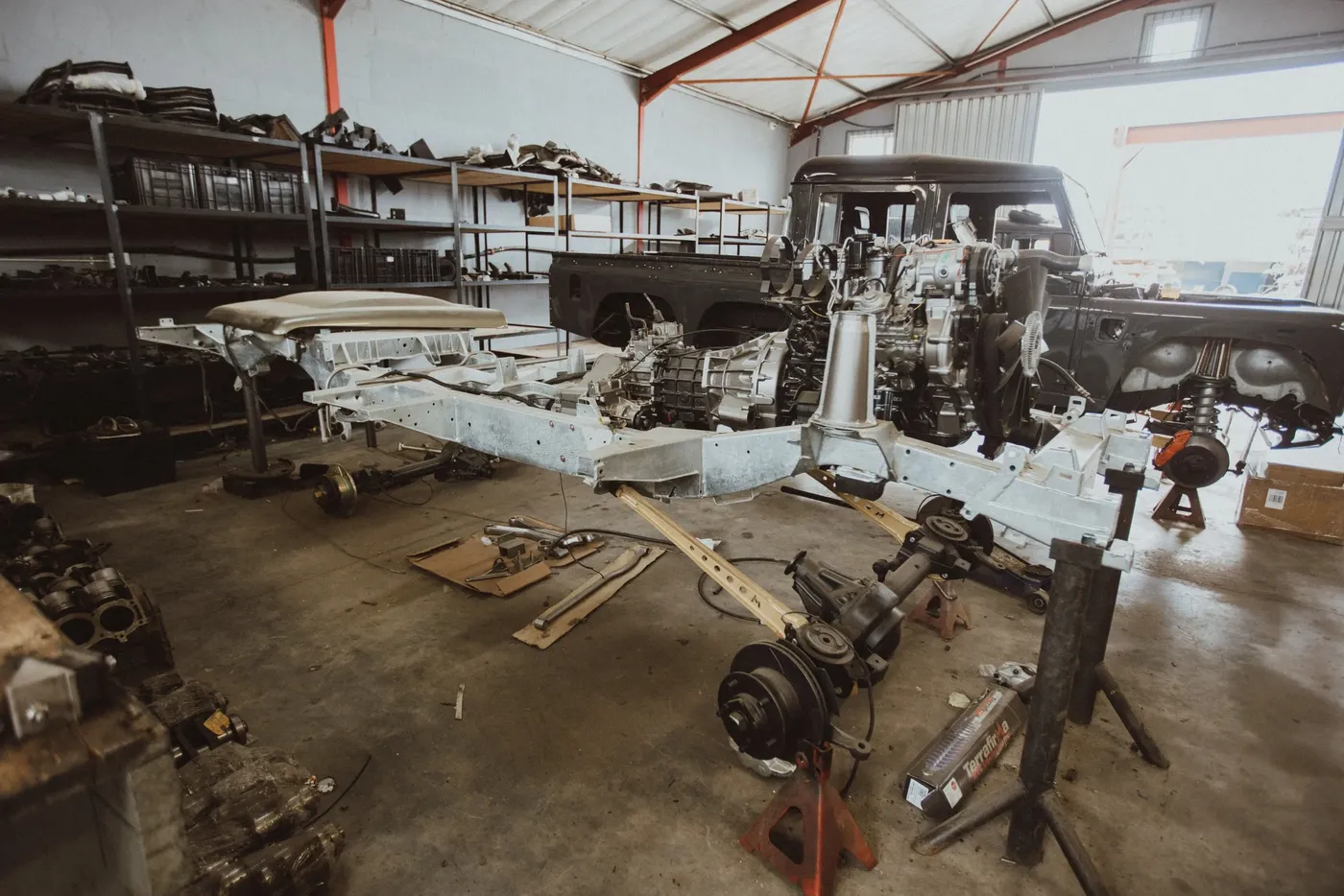 Stripped Land Rover Defender chassis, axles and components laid out in the workshop